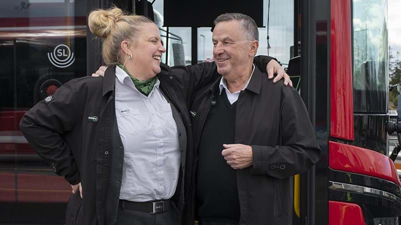 Två glada bussförare framför en röd SL-buss
